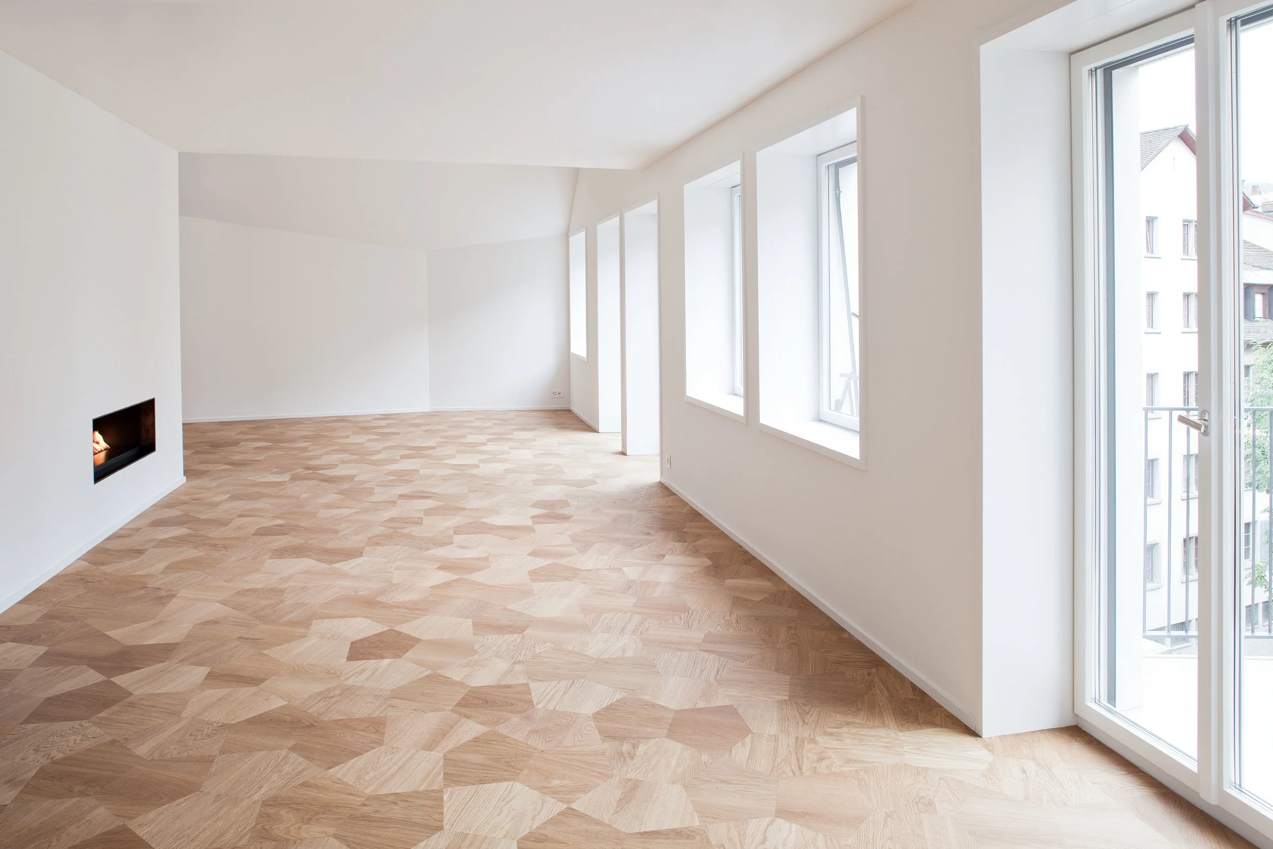 Geometrisches Parkettmuster in hellem Holz, lichtdurchfluteter Showroom-Raum mit Kamin und Panoramafenstern.